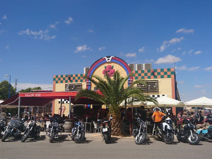 Fachada del Rolling Rock American Bar con la terraza llena y las motos aparcadas delante